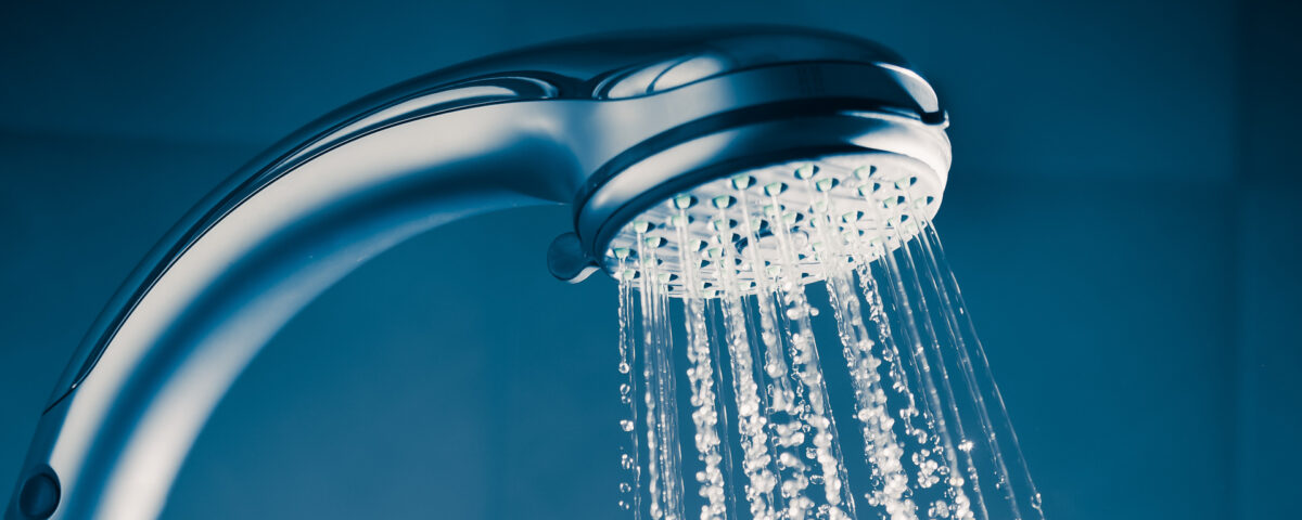 Close-up of a showerhead with water streaming down against a dark blue background.