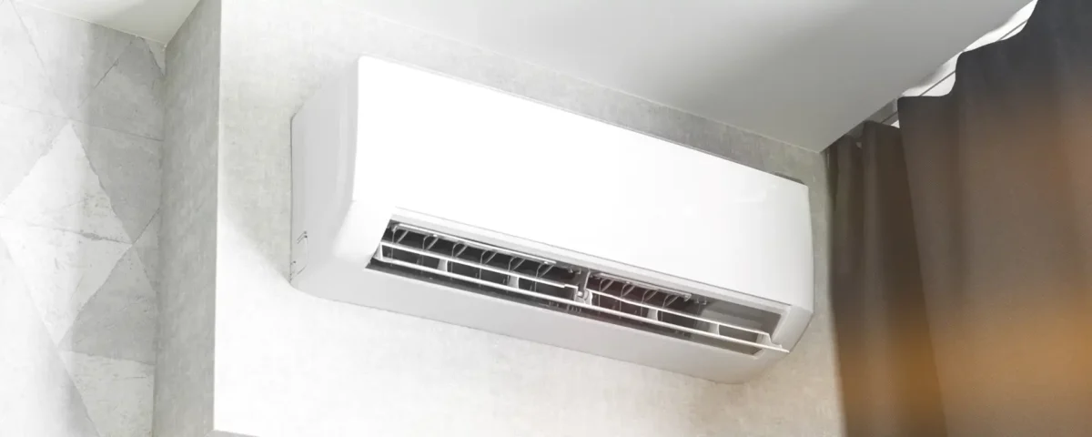Wall-mounted air conditioning unit in a room, with its vent open and positioned near a dark curtain.
