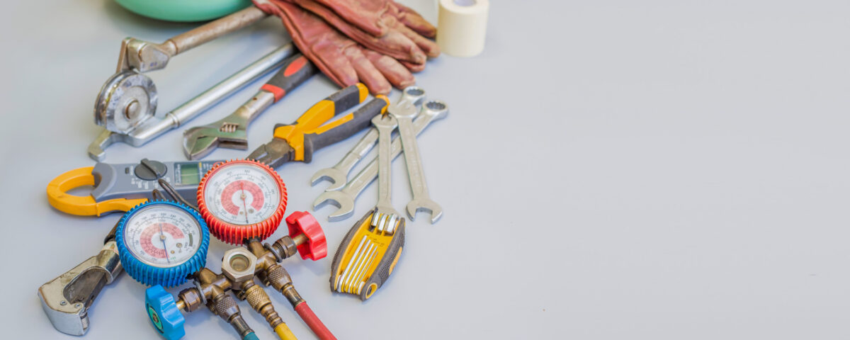 Assorted tools and workshop equipment, including gauges, pliers, wrenches, gloves, and an angle grinder, displayed on a gray surface.