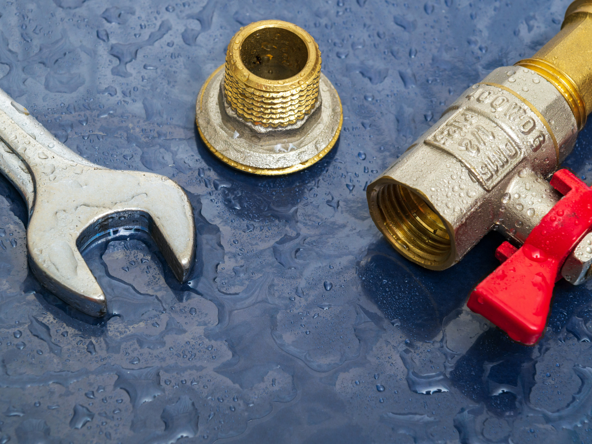 A wet wrench and a brass fitting next to a water valve with a red lever on a blue surface.