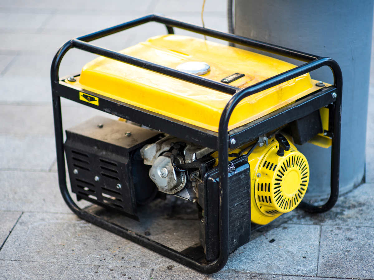 A yellow portable generator on a paved surface next to a gray pillar.
