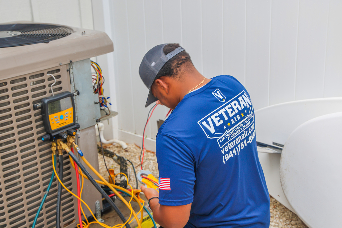 A technician in a “Veteran Air” shirt uses a tool to service an outdoor HVAC unit, with various wires and gauges attached to the equipment.