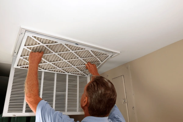 A person installs or replaces an air filter in a ceiling vent inside a room.