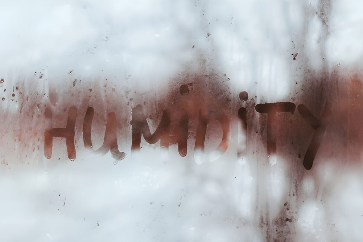 The word "HUMIDITY" is written with a finger on a foggy, condensation-covered glass surface.