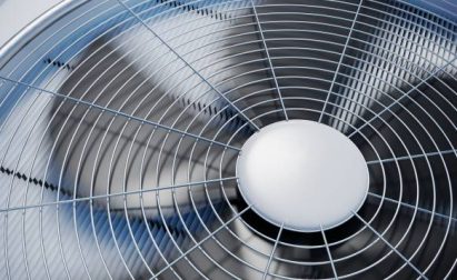 Close-up of a metal fan with spinning blades, enclosed by a circular wire grille.