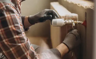 Person in plaid shirt and gloves expertly adjusting a valve on a radiator in the room, demonstrating skills akin to those used in dehumidifier repair.