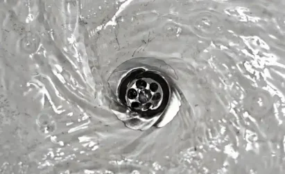 Water swirling down a silver sink drain, creating a visible vortex.