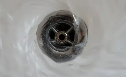 Water swirling down a metal drain, creating a whirlpool effect.