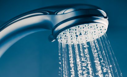 Close-up of a showerhead with water streaming down against a dark blue background.