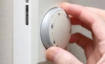 A hand adjusts a round, white thermostat on a wall.