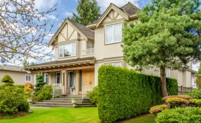 A two-story house with large windows, wooden accents, and a manicured lawn surrounded by hedges and trees under a blue sky features top-notch HVAC services by Veteran Air Sarasota.