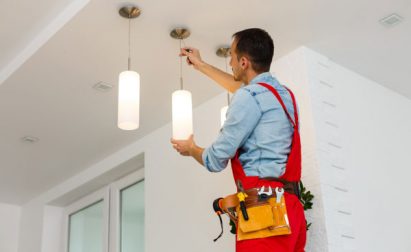 Person in red overalls adjusting a ceiling light fixture.