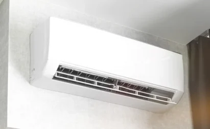 Wall-mounted air conditioning unit in a room, with its vent open and positioned near a dark curtain.