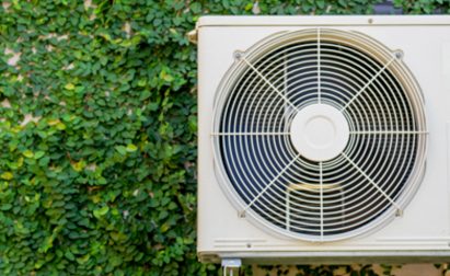 An outdoor air conditioning unit mounted on a wall covered with dense green ivy leaves.