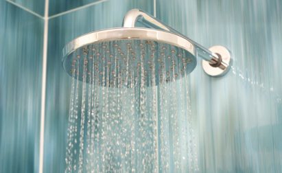 A showerhead releasing water streams in a tiled bathroom setting.