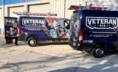 Two service vans labeled "Veteran Air" with eagle mascots are parked outside a building. A person stands near one van.