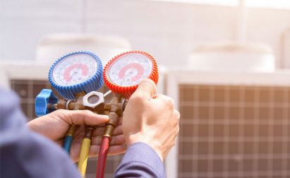 A person uses a pressure gauge manifold with blue and red dials to check HVAC equipment.