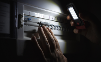 Hand holding a flashlight to illuminate a darkened electrical panel, focusing on adjusting circuit breakers.