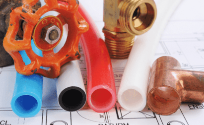 Various plumbing pipes and fittings lie on architectural blueprints, including copper fittings, valves, and colorful pipes.