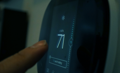 A hand adjusts a digital thermostat set to 71 degrees Fahrenheit.