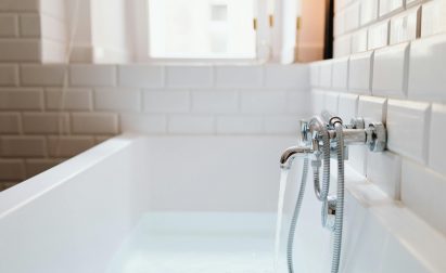Bathtub with running water and chrome fixtures in a tiled bathroom.