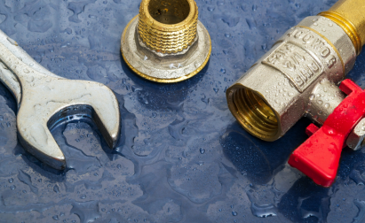 A wet wrench and a brass fitting next to a water valve with a red lever on a blue surface.