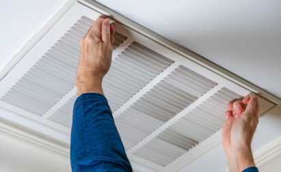 Person wearing a blue sleeve adjusting a ceiling air vent cover with both hands.