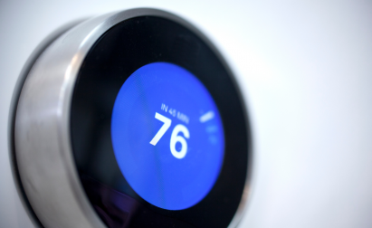 Close-up of a smart thermostat with a stainless steel frame displaying a temperature of 76 degrees on a blue digital screen.