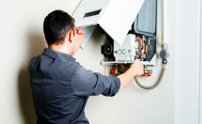 Person inspecting an open wall-mounted boiler unit, adjusting components with one hand, in a well-lit room.
