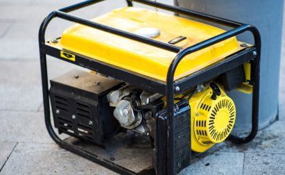 A yellow portable generator on a paved surface next to a gray pillar.